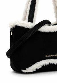 Sac en daim noir avec une finition blanche et duveteuse, doté de deux poignées en cuir noir et d'une marque dorée à l'avant. Design compact et structuré.