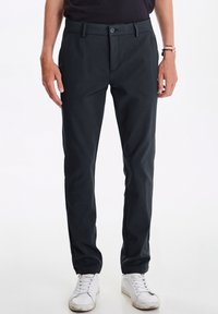 Dark gray trousers made of woven fabric, featuring a flat front, front pockets, and a slim fit design. Paired with white sneakers.