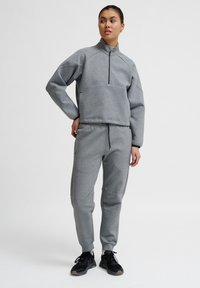 Pullover in fleece grigio con colletto alto e zip a metà, abbinato a joggers aderenti coordinati. L'outfit presenta una texture morbida e polsini elasticizzati.