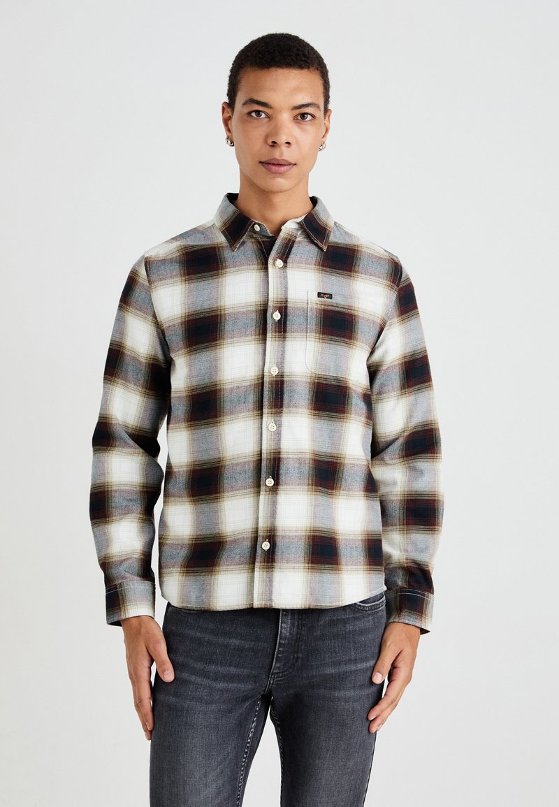 Camisa de franela de botones con un patrón de cuadros en blanco, gris y marrón oscuro. Cuenta con un cuello, mangas largas y un bolsillo en el pecho.