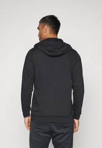 Sudadera con capucha negra de textura suave, de manga larga y con ribete en el dobladillo, con un ajuste relajado y costuras en la parte posterior.