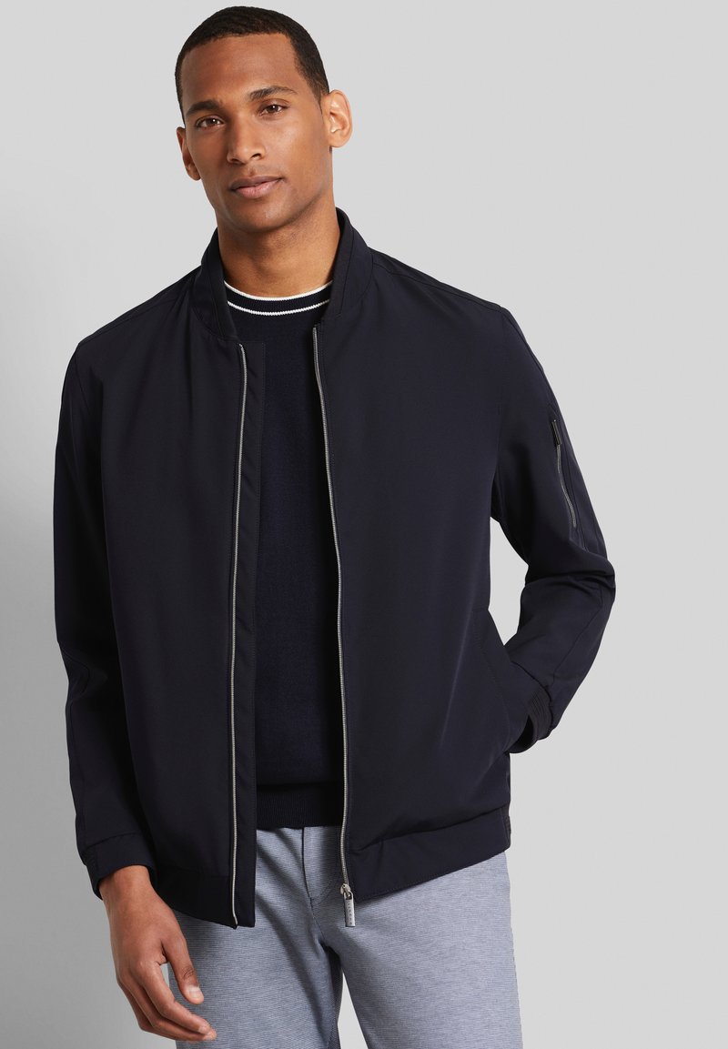 Blouson de pilote de marine avec fermeture éclair sur le devant, poignets côtelés et col montant. Tissu lisse avec un léger brillant et détails de poches zippées sur les côtés.