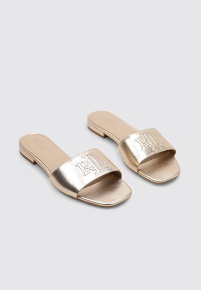Sandalias metálicas doradas con una tira ancha que presenta un logo en relieve, punta cuadrada y tacón bajo en bloque. Textura suave con un acabado brillante.
