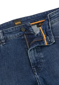 Mörkblå denimjeans med dragkedja, knappstängning och orange sömnadsaccent på midjebandet och fickans insida.