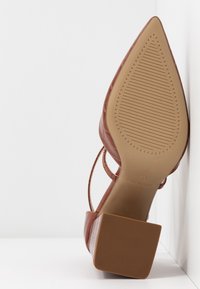 Braunes Lederhochhackerschuh mit spitzer Zehe, strukturiertem Obermaterial und einem quadratischen, gemusterten Absatz. Flache Sohle mit gerippten Details.