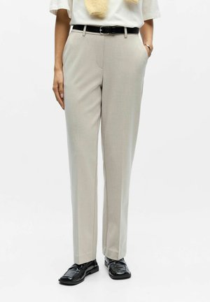 Light beige trousers with a tailored fit, flat front, and waistband. Paired with shiny black shoes. Textured fabric, clean lines, minimal details.