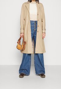 Manteau en cuir beige avec un design double boutonnage, associé à un jean flare taille haute bleu clair et un petit sac orange.
