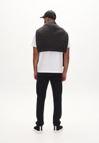 Dunkelgrauer gestrickter Pullover, drapiert über einem weißen T-Shirt, kombiniert mit schwarzen Hosen und blauen Sneakers. Rückansicht, minimalistischer Hintergrund.