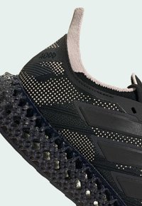 Black athletic shoe featuring a textured knit upper and translucent, lattice-style midsole. Accents in light pink and embossed logo detail.