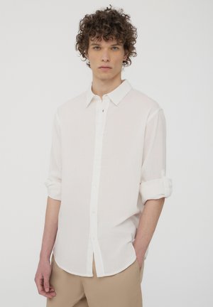 Camicia bianca a maniche lunghe con colletto a bottoni, realizzata in tessuto leggero. Presenta maniche arrotolate e orlo dritto.