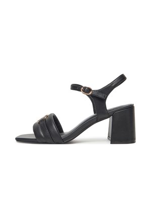 Sort sandal med åben tå med bred rem, ankelrem med guldlås og blokhæl på hvid baggrund.