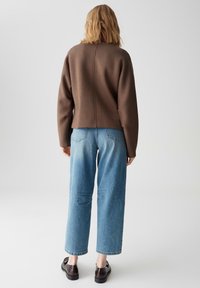 Maglione a maglia marrone con una vestibilità rilassata, abbinato a jeans di denim blu chiaro con gamba dritta e lavaggio leggermente sbiadito. Scarpe nere visibili.