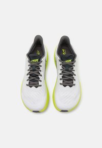 White athletic shoes with gray laces, mesh upper, and neon green outsole. Features a sleek design and textured surface for grip.