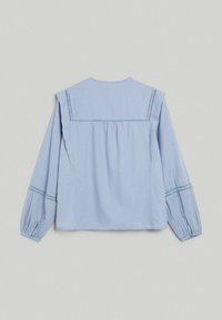 Hellblaue Bluse mit langen Ärmeln, detaillierten Nähten an Schultern und Bündchen, weichem Stoff und lockerem Schnitt.