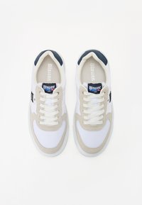 Hvite og beige joggesko med en glatt stoffoverdel, snøring og marineblå detaljer. Har polstret krage og teksturert såle.