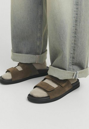 Sandales en suède marron avec une semelle noire, dotées de deux brides réglables. Portées avec un jean gris clair légèrement ample, retroussé.