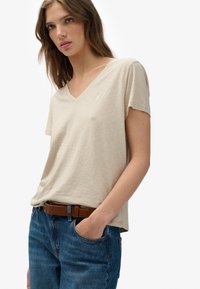 Beige V-hals T-shirt met korte mouwen, gemaakt van zachte stof, gecombineerd met blauwe jeans en een bruine riem, met een subtiele logodetail.