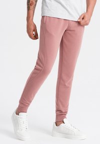 Helle rosa Sweatpants aus weichem Stoff, mit schmaler Passform, Seitentaschen und gerippten Bündchen, kombiniert mit weißen Sneakers.