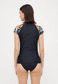 Black short-sleeve rash guard featuring a floral pattern on the sleeves. Smooth, stretchy fabric designed for comfort and sun protection.