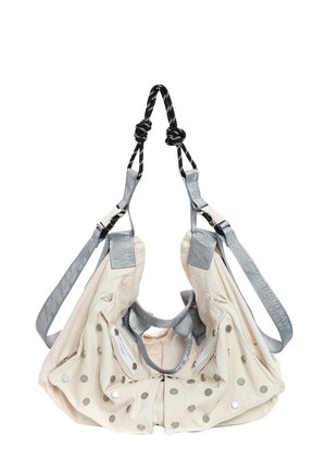 Bolso bandolera de tela beige con correas grises, botones de presión metálicos y asas de cuerda negra y blanca anudadas, mostrado sobre un fondo blanco.