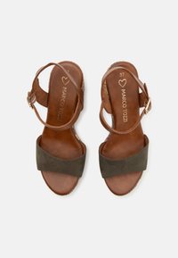 Sandales en cuir marron avec une large sangle en daim vert foncé. Elles disposent d'une sangle de cheville avec une boucle et d'une semelle intérieure texturée. Taille 37.