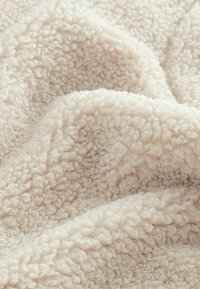 Tissu en peluche crème avec une surface douce et texturée, présentant un motif ondulé en boucles, créant une apparence cosy et chaleureuse.
