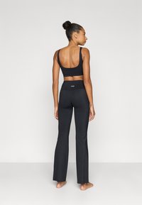 Μαύρο αθλητικό μπουστάκι με φαρδιές τιράντες, συνδυασμένο με μαύρο κολάν υψηλής μέσης με καμπάνα. Λείο ύφασμα, minimal λογότυπο στη μέση.