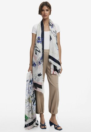Blumenmuster-Schal aus leichtem Stoff in Marine- und Pastelltönen, stilvoll drapiert. Ergänzt durch beige Jogginghosen und blaue High Heels.