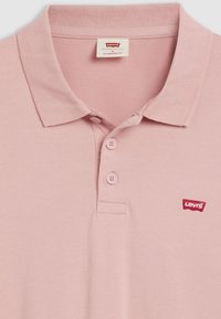 Polo en coton rose avec col, doté de trois boutons et d'un petit logo Levi's rouge sur la poitrine. Coupe standard.