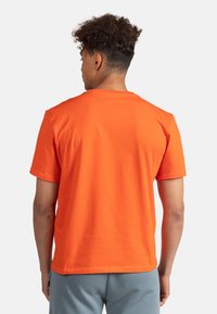 T-shirt a maniche corte in cotone arancione brillante, con collo rotondo e una vestibilità comoda. Tessuto liscio con un colore uniforme, senza stampe o dettagli.