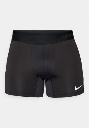 Fekete sportnadrág rugalmas anyagból. Széles fekete derékpánttal rendelkezik, rajta a "NIKE PRO" logóval és egy fehér Nike pipa emblémával az oldalon.