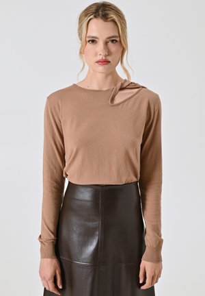 Top lungo maniche marrone con un design unico di ritaglio sulla spalla, realizzato in un tessuto morbido. Abbinato a una gonna in pelle nera aderente.