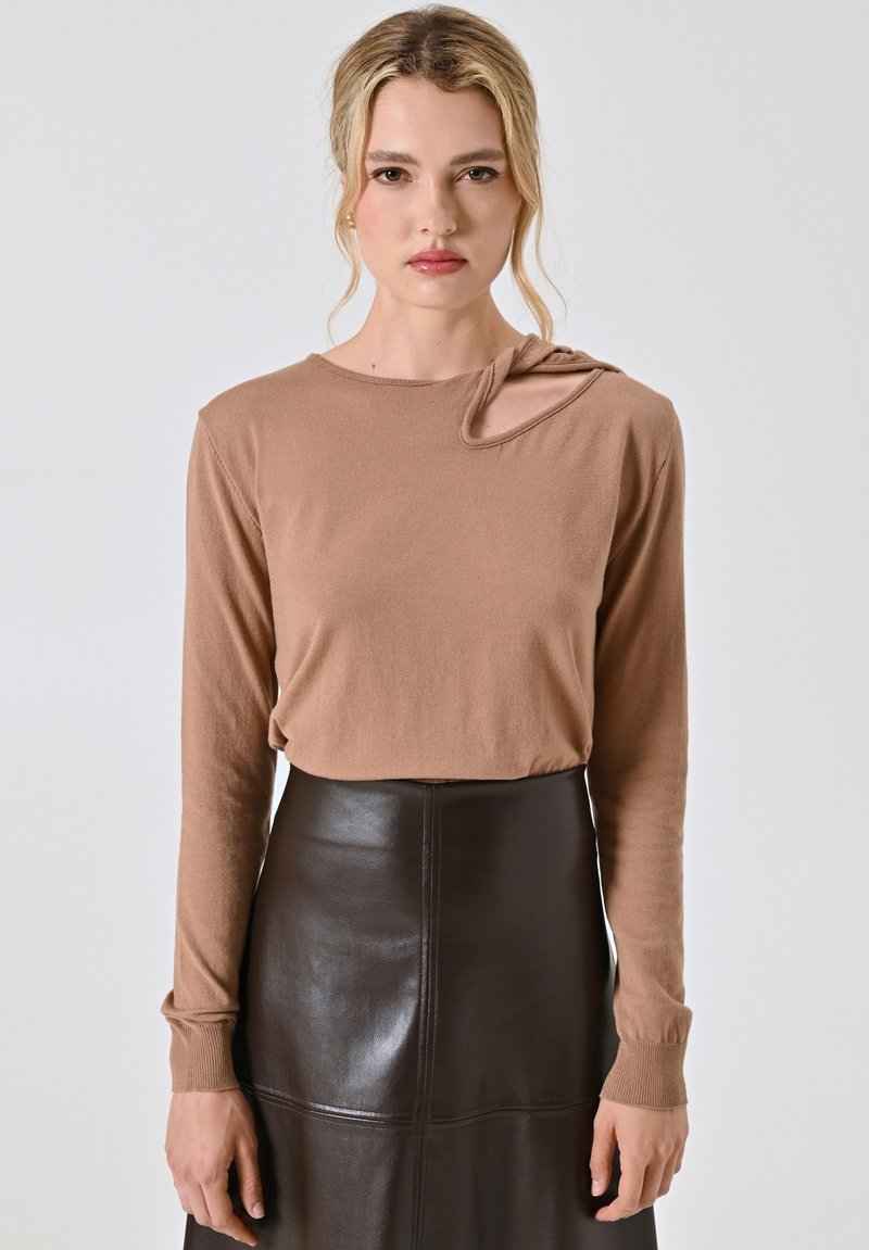 Top lungo maniche marrone con un design unico di ritaglio sulla spalla, realizzato in un tessuto morbido. Abbinato a una gonna in pelle nera aderente.