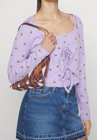 Lila kortärmad tröja med orange blommönster, med en frontdetalj i form av knyt; parat med en jeanskjol och en mönstrad brun handväska.