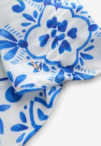 Witte stof met een blauw bloemenpatroon, met een klein zilveren hardwaredetail. Het ontwerp bevat bladeren en hartvormen.