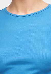 Κοντινό πλάνο ενός ατόμου που φοράει μπλε ριμπ πουκάμισο με στρογγυλή λαιμόκοψη, δείχνοντας τον λαιμό και την άνω περιοχή του στήθους.