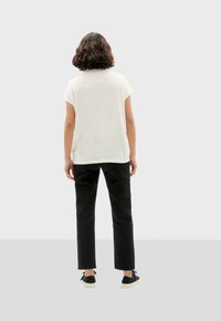 Witte top met korte mouwen, zwarte rechte broek en zwarte schoenen met lichte zolen. Minimalistisch ontwerp, gladde textuur en casual pasvorm.