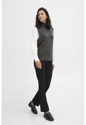Dunkelgraues, geripptes, ärmelloses Oberteil über einem weißen Langarmshirt, kombiniert mit schwarzen, maßgeschneiderten Hosen und schwarzen Slippern. Glatte Textur, strukturiertes Design.