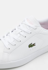 White leather sneaker with round toe, flat laces, embroidered green crocodile logo and subtle pink branding on the tongue. Textured rubber sole.