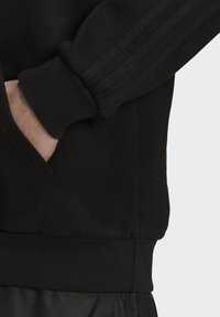 Sort sweatshirt med ribbede manchetter og kant, med teksturerede striber langs ærmerne. Stoffet ser blødt og strækbart ud.