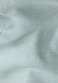 Hellblauer strukturierter Stoff mit einem Rastermuster, der eine weiche, unebene Oberfläche zeigt, die sich natürlich faltet und fällt.