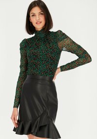 Zielona bluzka w panterkę z przezroczystymi długimi rękawami i wysokim dekoltem. Czarna spódnica z sztucznej skóry z falbaną i detalami w stylu kopertowym z przodu.