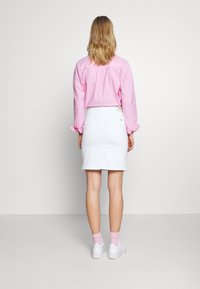 Chemise rose clair à manches longues avec des poignets retroussés, associée à une jupe en denim blanche, dotée de poches arrière et d'une étiquette à la taille.