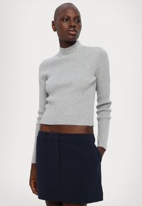 Maglione grigio a coste con collo alto e maniche lunghe, dal design corto. Abbinato a una mini gonna blu navy su misura con tasche.