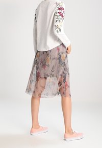 Top gris de manga larga con bordado floral en las mangas, combinado con una falda plisada y translucida de color rosa claro con un patrón floral y zapatillas rosas.