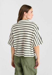 Gebreide top met horizontale zwart-witte strepen, korte mouwen en een gestructureerde stof. Achteraan is de contrasterende kleur en kraag zichtbaar.