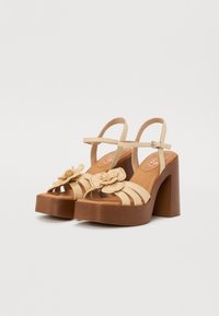 Beige plattform sandaler med en tykk brun hæl. Funksjoner inkluderer åpen tå-design, tynne stropper og en teksturert blomst accent på fronten.