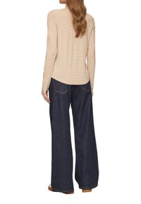 Langsleeve gestreepte top in beige en crème, gecombineerd met wijde donkerdenim jeans. De top heeft een ronde hals, een gladde textuur en aangesloten mouwen.