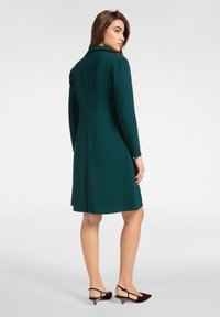 Ciemnozielona sukienka z długimi rękawami, miękka tekstura, prosty krój i kołnierzyk. Połączona z ciemnobrązowymi szpilkami. Prosty i elegancki design.
