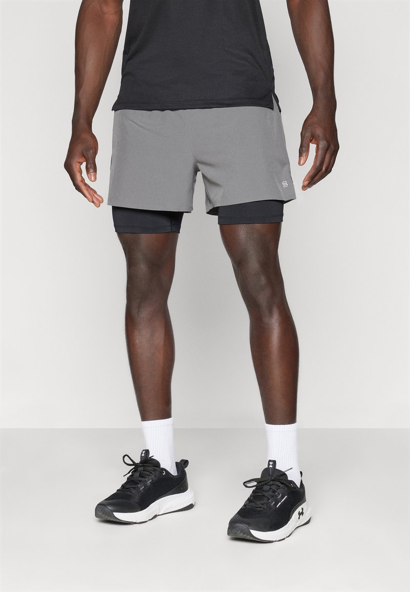 Grå atletiska shorts med svart foder, i kombination med svarta sneakers och vita strumpor. Enkelt design, lättviktigt tyg, inga synliga mönster.